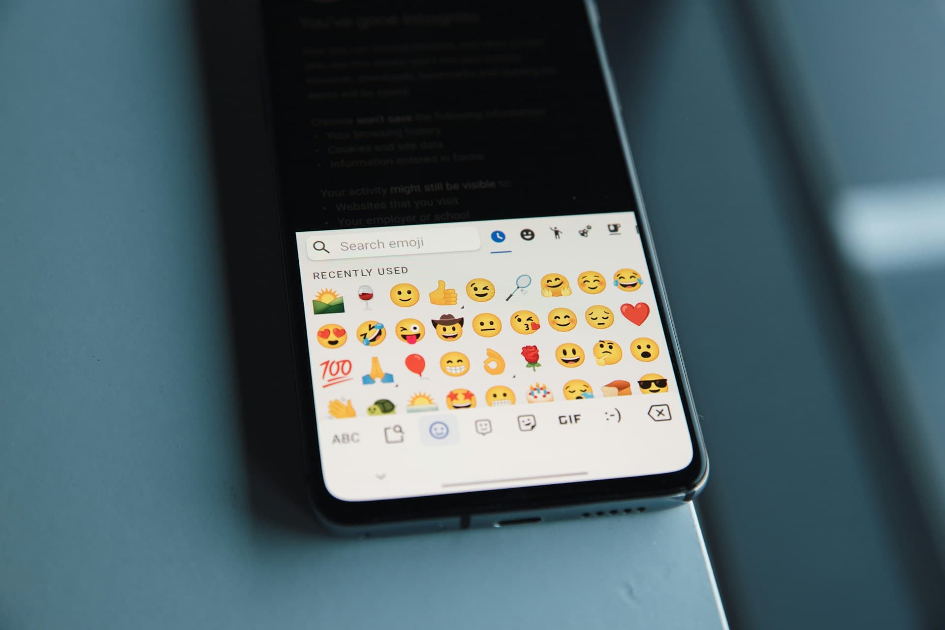机の上に置かれたスマートフォンのキーボードに絵文字の一覧が表示されている写真